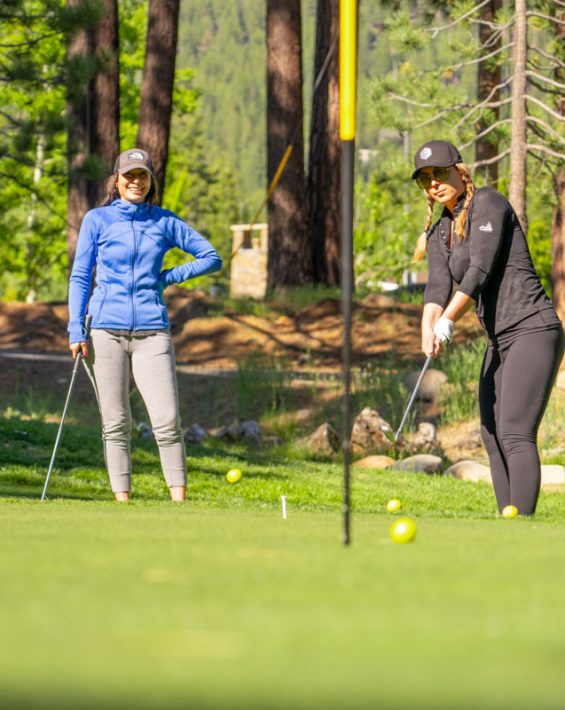 women chipping on practice green