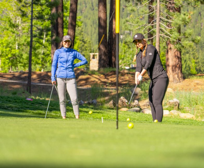 women chipping on practice green