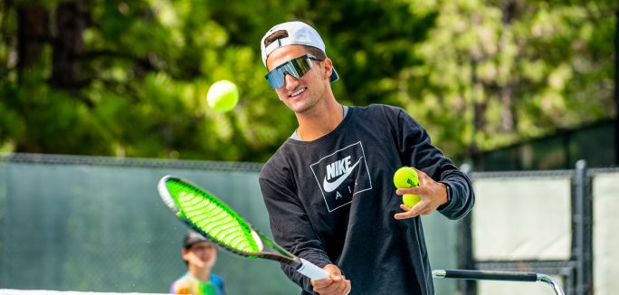young man holding a tennis racket hitting a tennis ball