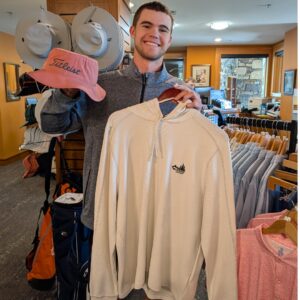 golf shop merchandise staff dads and grads pick kai holds up a long sleeve and hat
